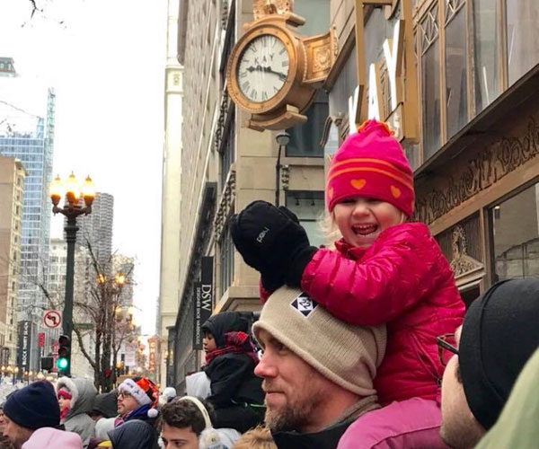 girl smiling on dad's shoulders while watching parade in Chicago