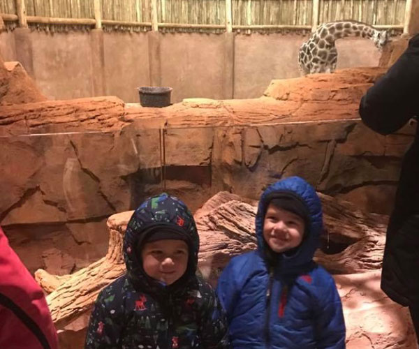 kids smiling outside giraffe exhibit at the zoo