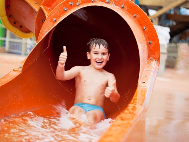outdoor waterpark boy giving thumbs up in waterslide