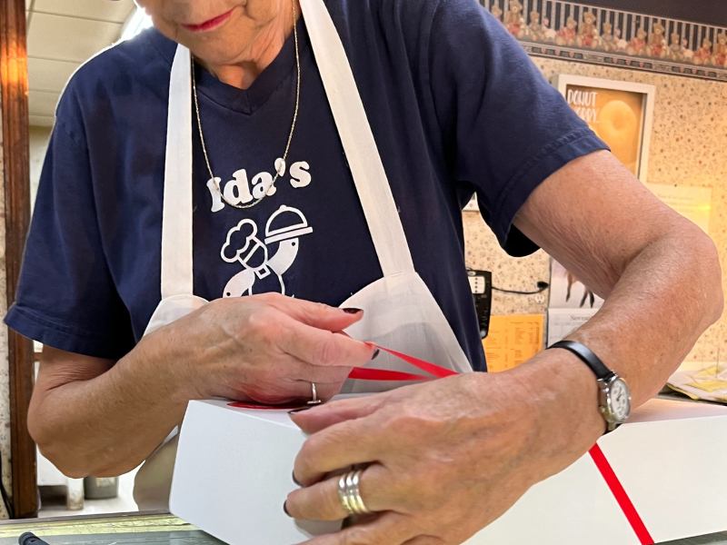 Ida's Pastry Shoppe employee wrapping the donuts I bought with a red ribbon