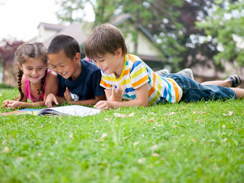 summer reading program kids reading book in grass