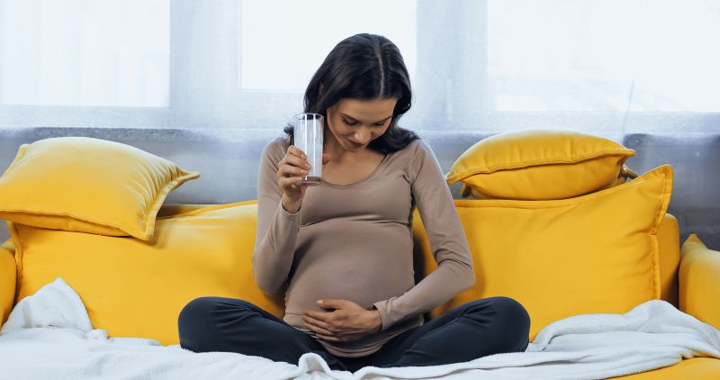 pregnant woman drinking milk on couch