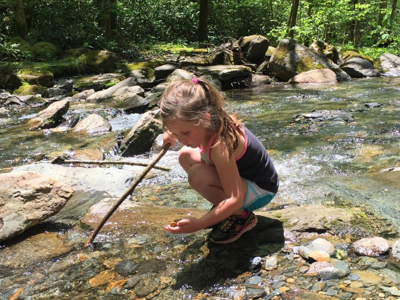 little girl crouches in a river for a closer view of river rocks in the Smoky Mountains.