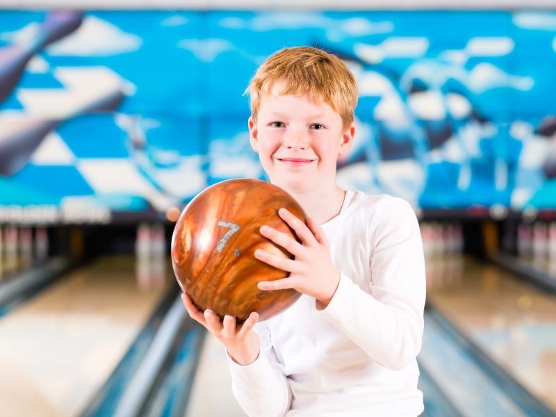 kids bowl free boy holding ball in front of lanes canva Kzenon
